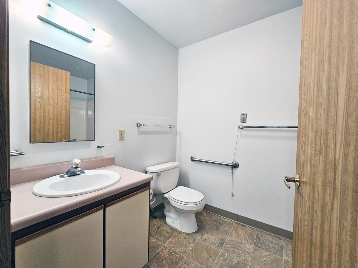 Dated apartment bathroom with a coloured vanity top and worn flooring before renovation.