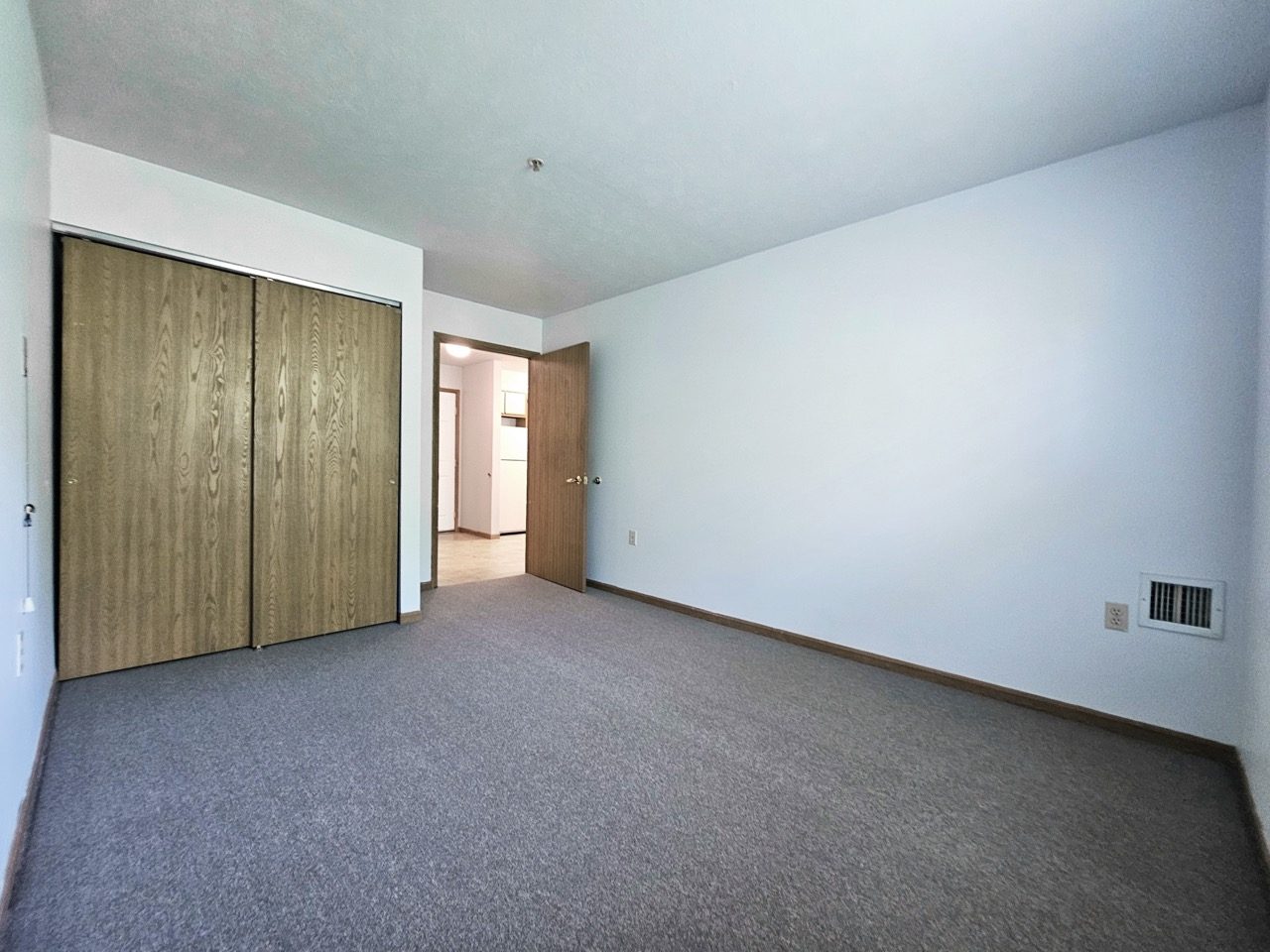 An empty apartment with dark worn carpet and dated closet doors before renovation.