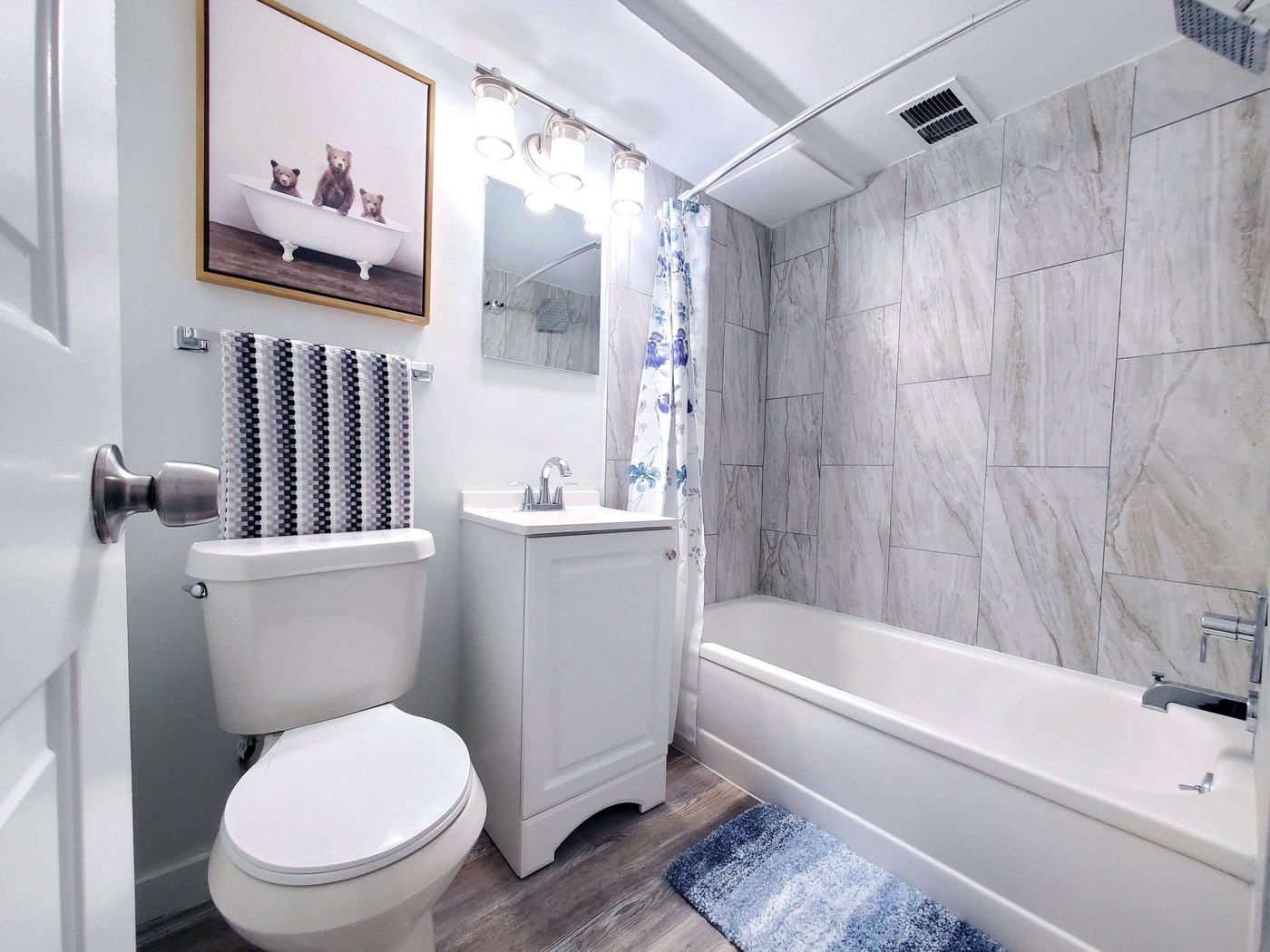 Renovated apartment bathroom with marble-look tile surround, new vanity and fixtures.